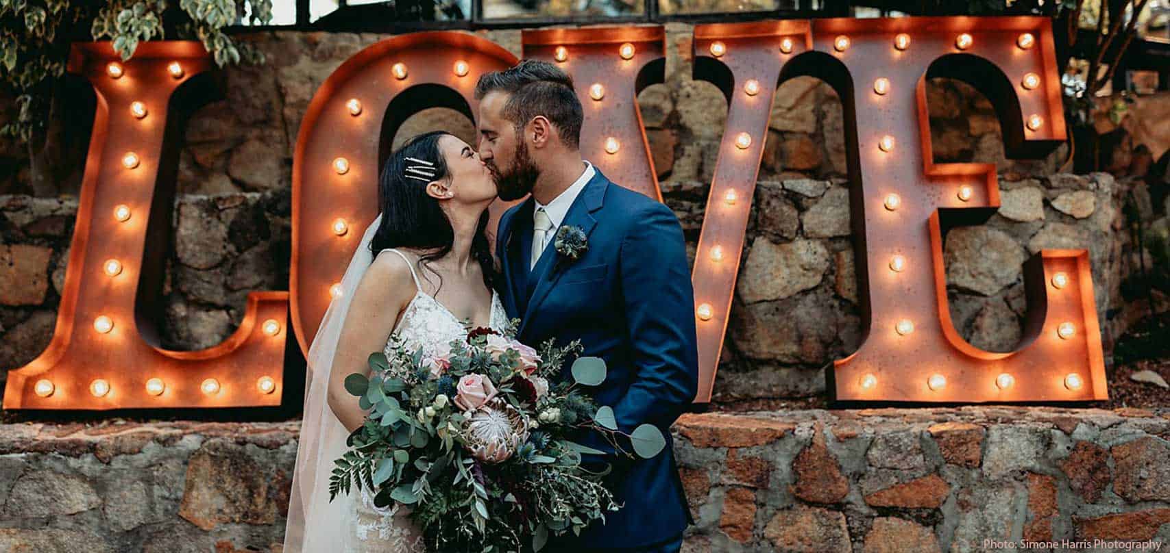 A bride and groom kissing in front of giant light up LOVE letters.